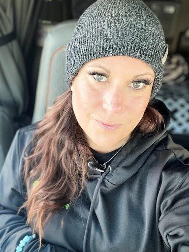 A brown haired woman with a grey beanie and black sweatshirt takes a selfie.